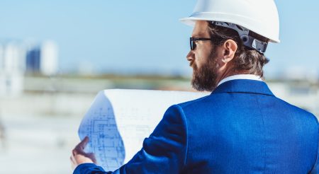 businessman-in-hardhat-and-suit-examining-building-plans